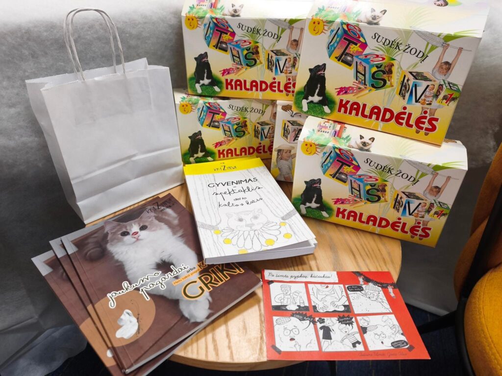 Ant stalo sudėtos bibliotekai Kalėdų proga padovanotos dovanos: vaikams skirtos knygos, komiksas, stalo žaidimai „Kaladėlės“ ir dovanų maišelis.