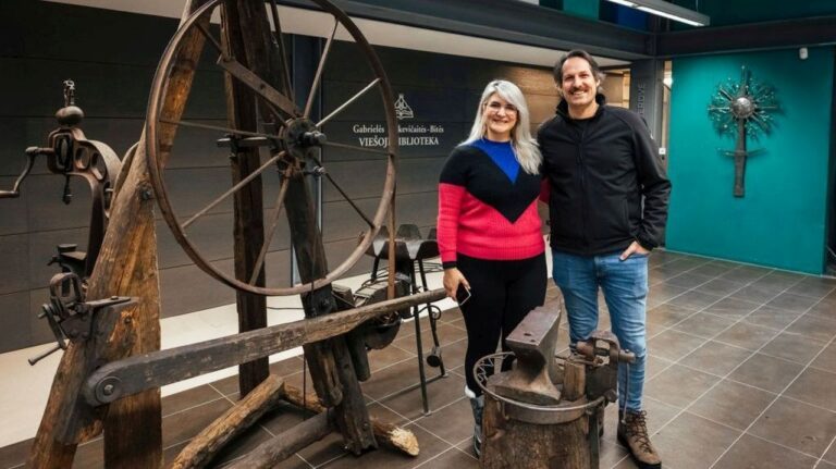 Moteris ir vyras stovi ir šypsosi kalvystės įrankių bibliotekos erdvėje fone