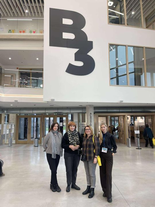 Keturios moterys renginio dalyvės pozuoja erdvaus vestibiulio fone