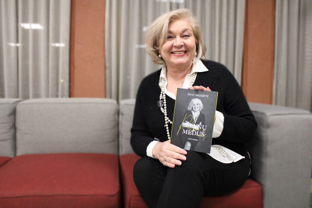 Ant sofos sėdi besišypsanti moteris, rankose laikanti knygą „Pelynų medus“. Ji vilki juodai baltus drabužius, ant kaklo – ilgi karoliai, fone matyti minkšti baldai ir užuolaidos.