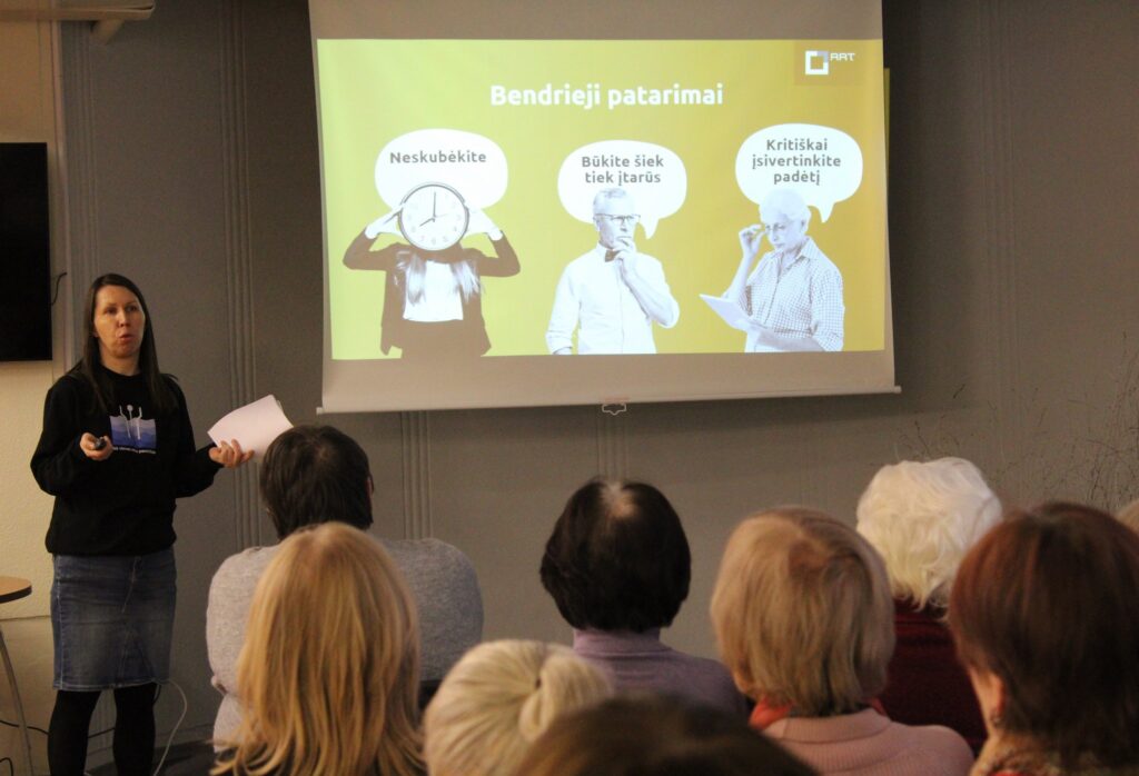 Moteris stovi prieš auditoriją ir skaito pranešimą, laikydama lapą rankoje. Už jos ekrane rodoma skaidrė su geltonu fonu ir antrašte „Bendrieji patarimai“, kurioje pavaizduoti trys žmonės su kalbos burbulais: „Neskubėkite“, „Būkite šiek tiek įtarūs“ ir „Kritiškai įsivertinkite padėtį“. Auditorijoje sėdi klausytojai, matomi iš nugaros.